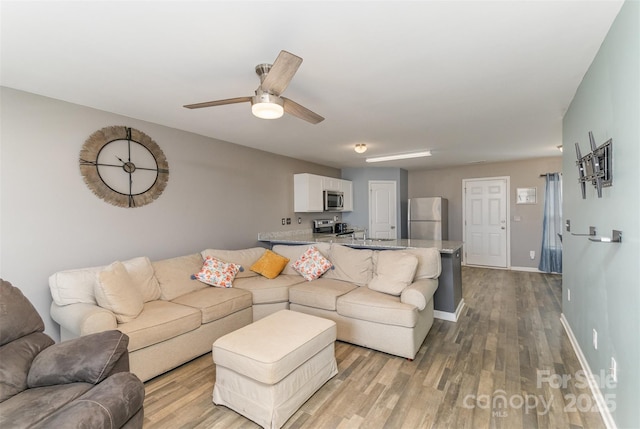 living area with light wood-type flooring, baseboards, and a ceiling fan