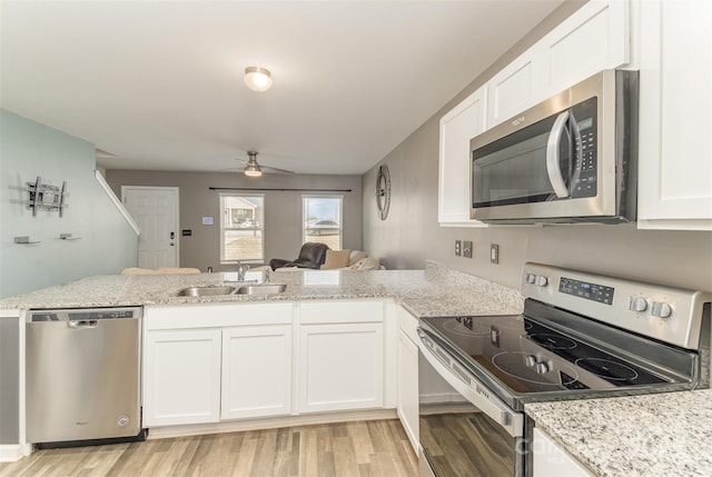 kitchen featuring a peninsula, a sink, white cabinets, appliances with stainless steel finishes, and light wood-type flooring