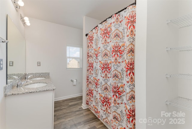 full bath with a shower with shower curtain, a sink, wood finished floors, baseboards, and double vanity