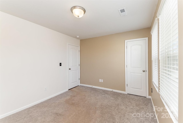 spare room with baseboards, visible vents, and light colored carpet