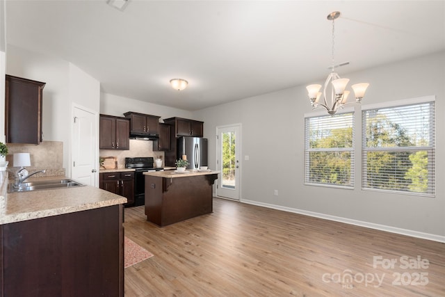 kitchen with black electric range oven, sink, stainless steel fridge, a kitchen island, and pendant lighting