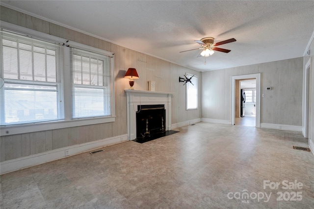 unfurnished living room featuring ceiling fan, wooden walls, and a textured ceiling