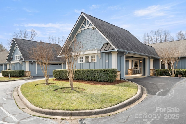 craftsman-style home featuring an attached garage, driveway, roof with shingles, board and batten siding, and a front yard