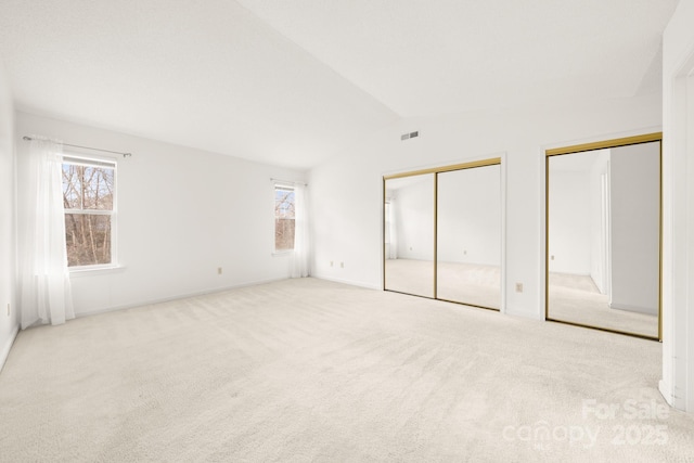 unfurnished bedroom featuring lofted ceiling, two closets, visible vents, and carpet flooring