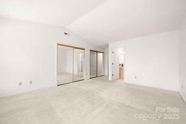 unfurnished bedroom with two closets, lofted ceiling, light colored carpet, visible vents, and baseboards