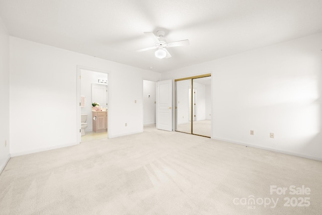 unfurnished bedroom with a closet, light colored carpet, ensuite bathroom, a ceiling fan, and baseboards