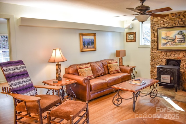 living room with ceiling fan, a wood stove, and light hardwood / wood-style floors