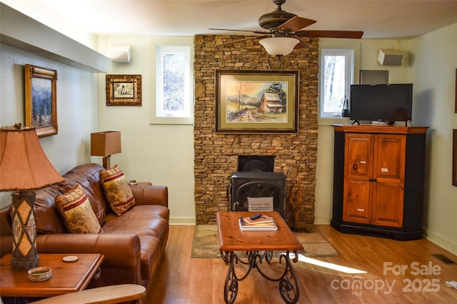 living room featuring an AC wall unit, a wood stove, ceiling fan, and light hardwood / wood-style flooring