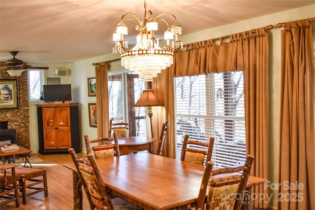 dining room with a wood stove, ceiling fan with notable chandelier, and light hardwood / wood-style floors