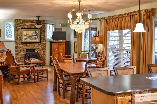 dining room featuring hardwood / wood-style flooring, plenty of natural light, a wood stove, and ceiling fan with notable chandelier