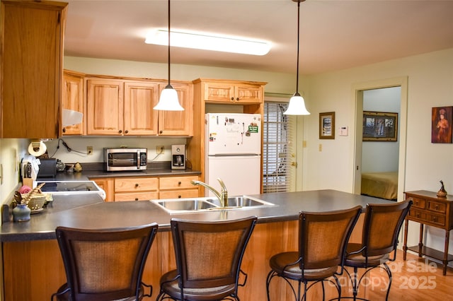 kitchen featuring decorative light fixtures, sink, a kitchen breakfast bar, white refrigerator, and light hardwood / wood-style floors