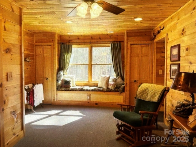 sitting room with wooden ceiling, carpet, a ceiling fan, and wood walls