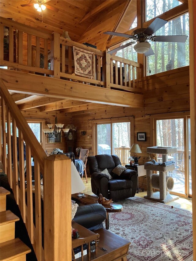 living room featuring wooden walls, wooden ceiling, stairway, vaulted ceiling, and ceiling fan with notable chandelier