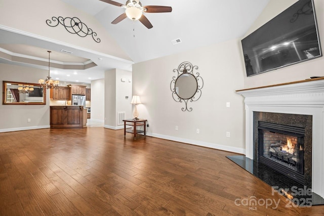 unfurnished living room featuring hardwood / wood-style flooring, a high end fireplace, ceiling fan with notable chandelier, vaulted ceiling, and a raised ceiling