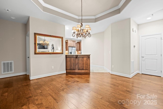 unfurnished dining area with ornamental molding, a raised ceiling, hardwood / wood-style floors, and a notable chandelier