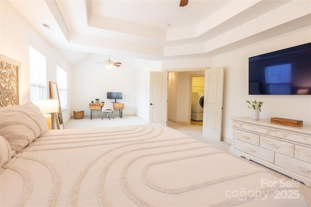 carpeted bedroom featuring washer / dryer, ceiling fan, and a tray ceiling