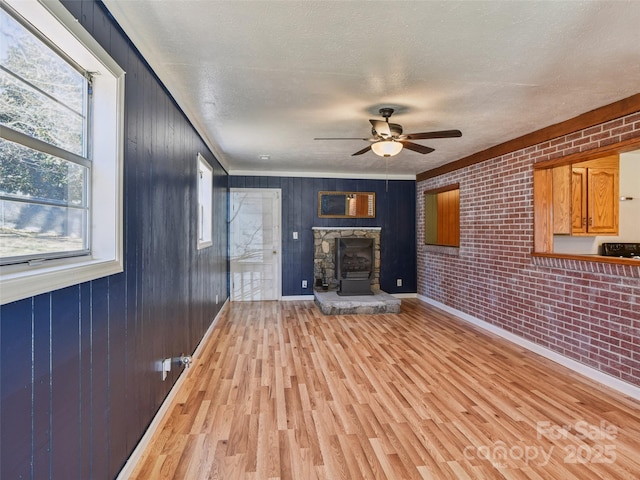 unfurnished living room featuring a textured ceiling, ceiling fan, a stone fireplace, brick wall, and light wood finished floors