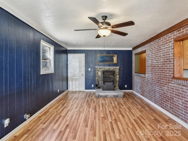 unfurnished living room featuring baseboards, brick wall, ceiling fan, wood finished floors, and a textured ceiling