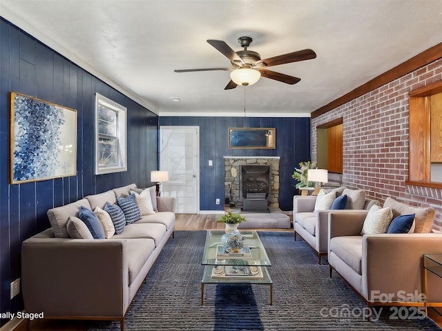 living area with brick wall, ceiling fan, wood finished floors, and a stone fireplace