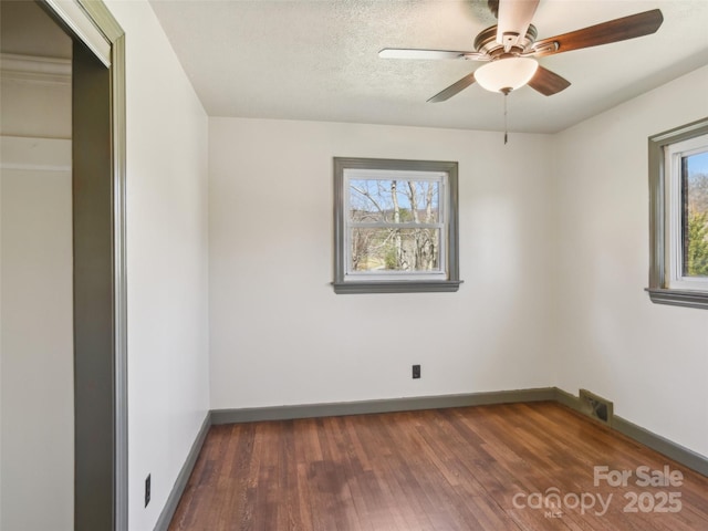 empty room with dark wood-style flooring, visible vents, ceiling fan, a textured ceiling, and baseboards