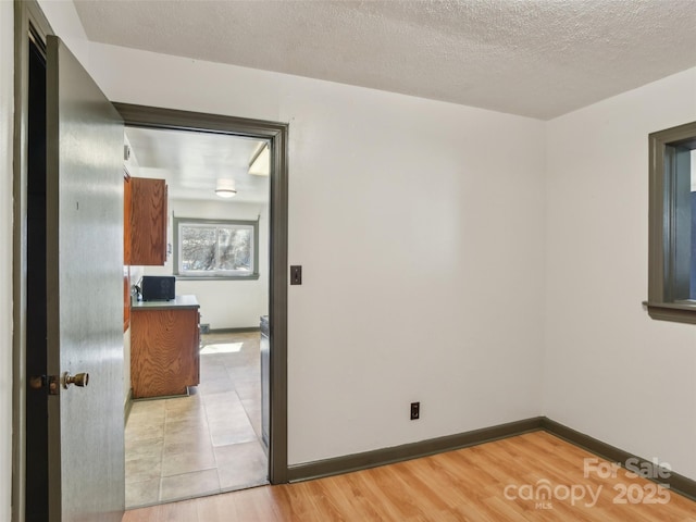 empty room with light wood-type flooring, baseboards, and a textured ceiling