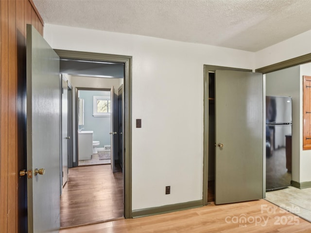 unfurnished bedroom featuring a textured ceiling, light wood-type flooring, and freestanding refrigerator