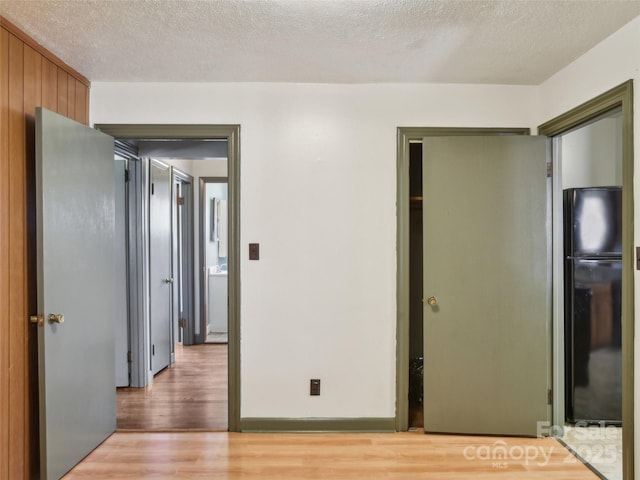 unfurnished bedroom featuring a textured ceiling, freestanding refrigerator, and light wood-style floors