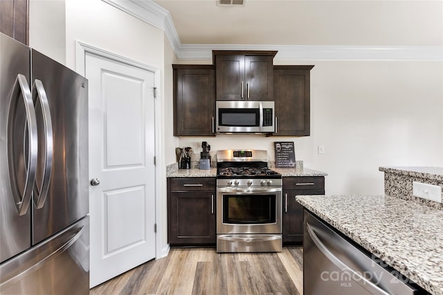 kitchen with dark brown cabinets, stainless steel appliances, light stone countertops, ornamental molding, and light wood-type flooring