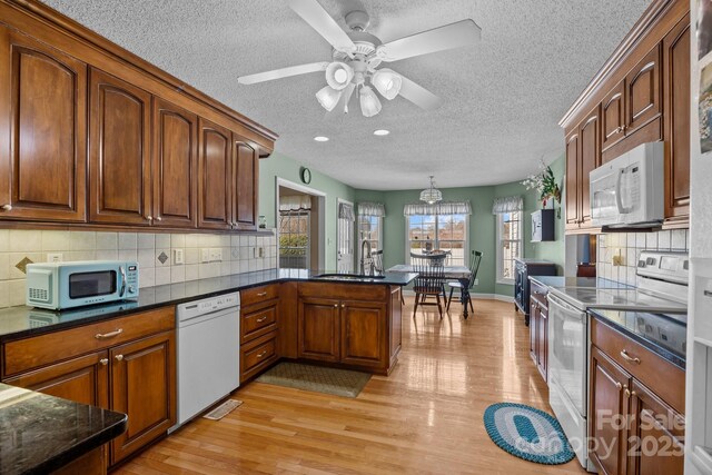 kitchen featuring pendant lighting, sink, white appliances, kitchen peninsula, and light wood-type flooring