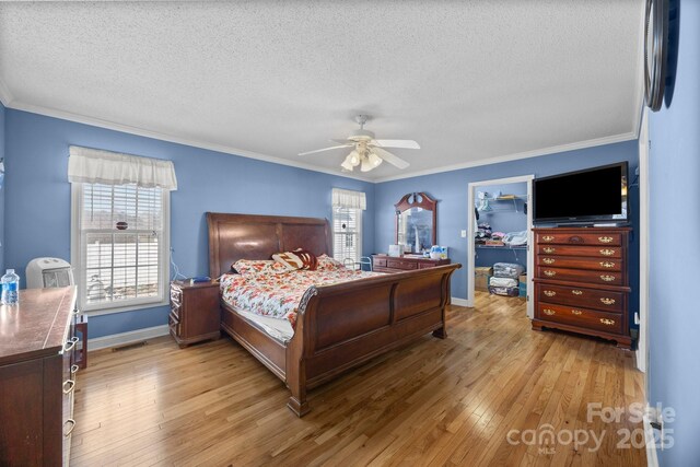 bedroom featuring a walk in closet, light hardwood / wood-style flooring, a textured ceiling, ornamental molding, and ceiling fan