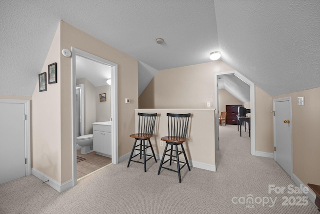 hallway with light carpet, lofted ceiling, and a textured ceiling