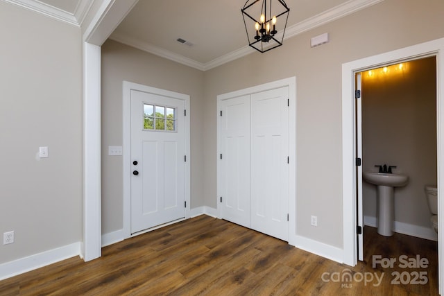 foyer entrance with crown molding, dark wood-type flooring, sink, and a notable chandelier