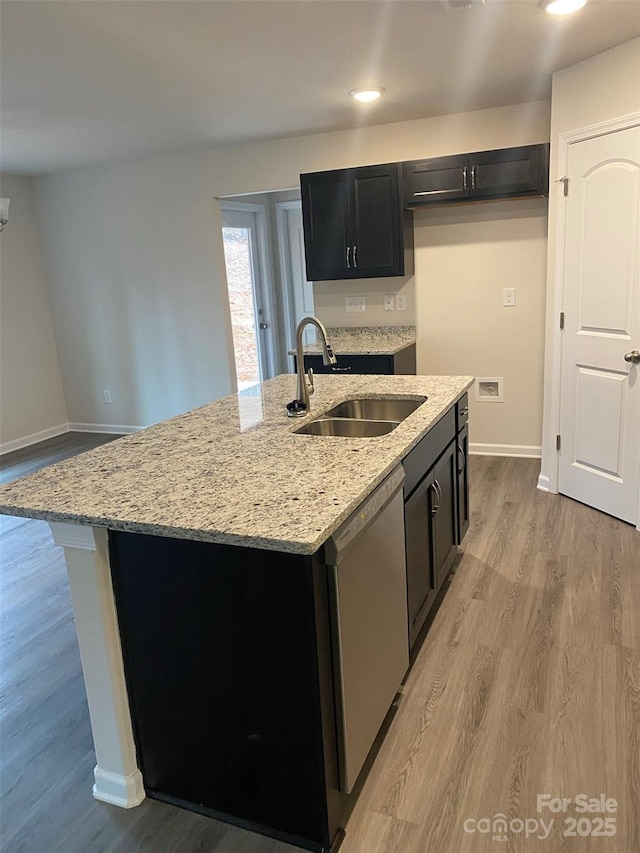 kitchen featuring sink, light stone counters, dishwasher, an island with sink, and light hardwood / wood-style floors