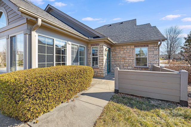 exterior space featuring stone siding, a shingled roof, and fence