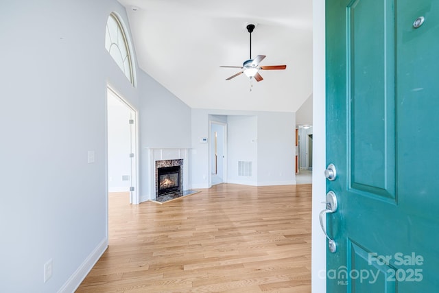 entrance foyer with visible vents, baseboards, light wood-style flooring, a premium fireplace, and ceiling fan