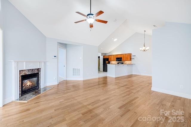 unfurnished living room with a fireplace, visible vents, light wood-style flooring, high vaulted ceiling, and ceiling fan with notable chandelier