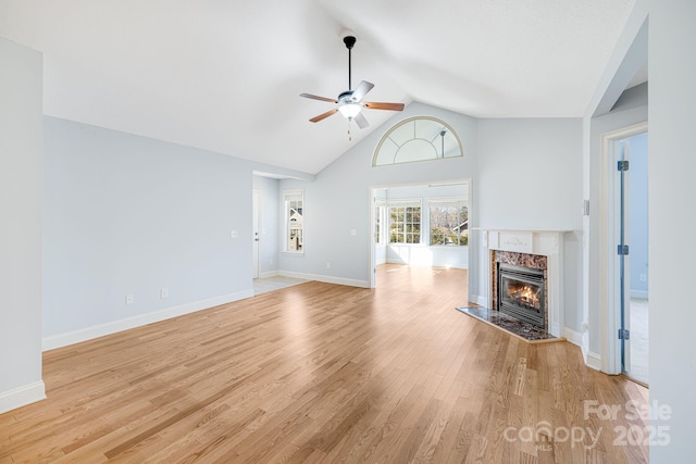 unfurnished living room with light wood finished floors, baseboards, ceiling fan, a premium fireplace, and vaulted ceiling