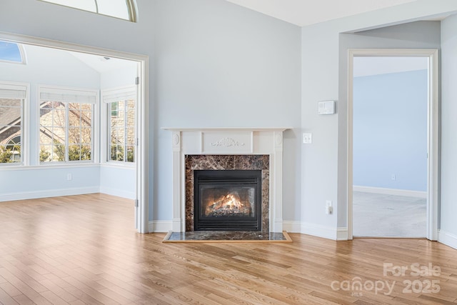 unfurnished living room featuring a premium fireplace, baseboards, and wood finished floors