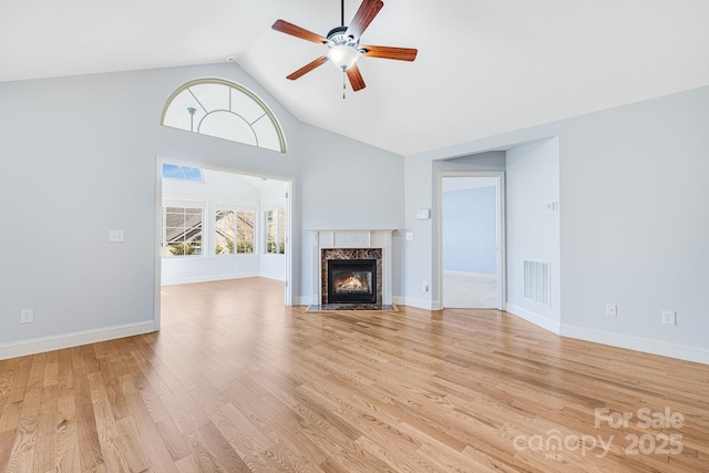 unfurnished living room with ceiling fan, a high end fireplace, visible vents, baseboards, and light wood finished floors