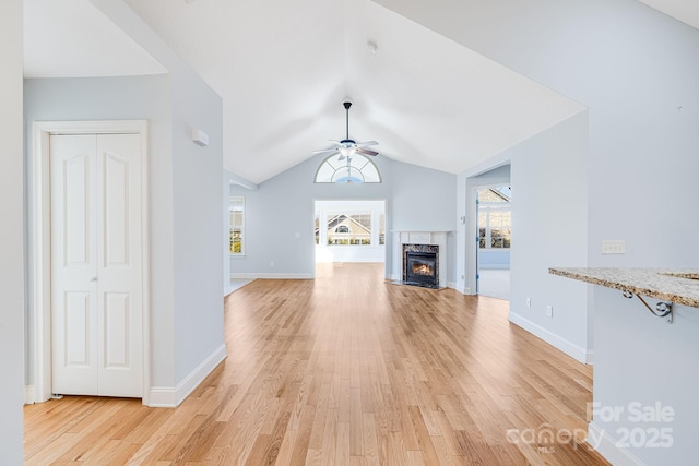 unfurnished living room featuring ceiling fan, a premium fireplace, baseboards, vaulted ceiling, and light wood-style floors