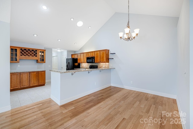 kitchen with light wood finished floors, glass insert cabinets, brown cabinets, a peninsula, and black appliances