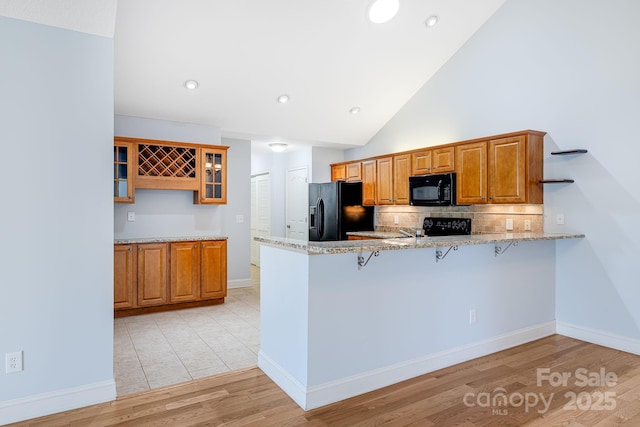 kitchen featuring a peninsula, black appliances, glass insert cabinets, and light stone countertops