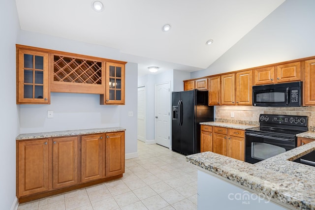 kitchen with lofted ceiling, glass insert cabinets, brown cabinets, light stone countertops, and black appliances