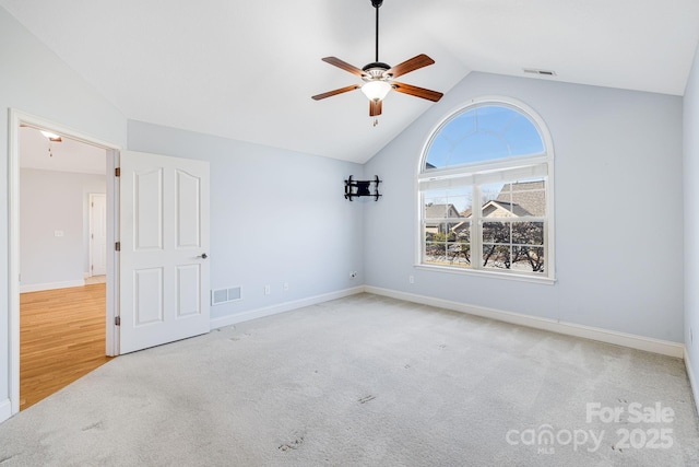 carpeted spare room with lofted ceiling, baseboards, visible vents, and a ceiling fan