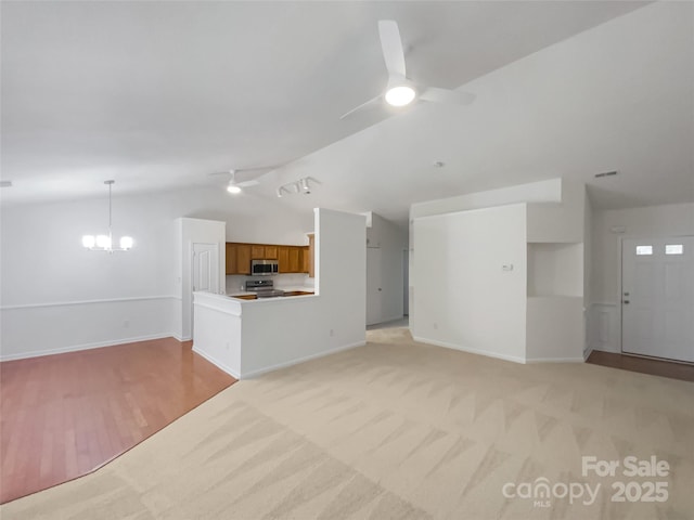 unfurnished living room with lofted ceiling, ceiling fan with notable chandelier, and light carpet