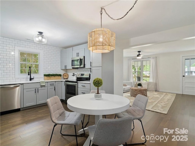 kitchen with dark wood-type flooring, stainless steel appliances, decorative light fixtures, and backsplash