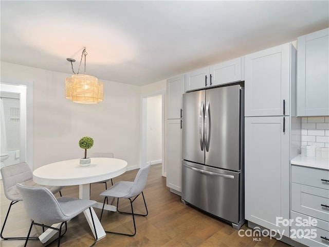 kitchen featuring wood-type flooring, stainless steel fridge, pendant lighting, decorative backsplash, and white cabinets