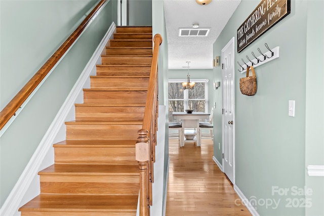 stairway with hardwood / wood-style floors, a textured ceiling, and a notable chandelier