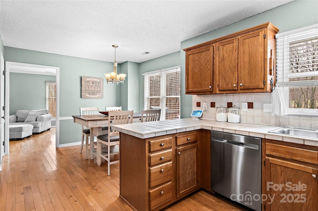 kitchen with hanging light fixtures, tile counters, stainless steel dishwasher, and kitchen peninsula