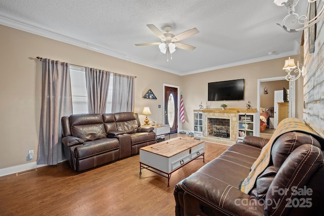 living room featuring a tile fireplace, hardwood / wood-style floors, ornamental molding, ceiling fan, and a textured ceiling